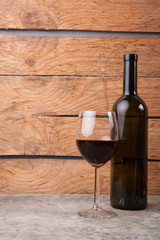 A wine bottle and near it a glass half filled with wine on wooden background