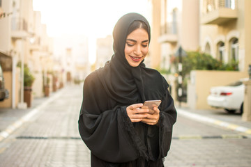 Young muslim woman using smart phone on the city street.