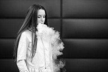 Vape teenager. Young pretty white girl in casual clothing smoking an electronic cigarette opposite modern background on the street in the spring. Bad habit. Vaping activity. Close up. Black and white.