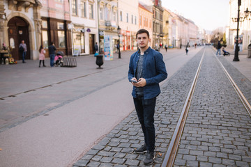 Young stylish man stand in centre of the city. Man use wireless headphones