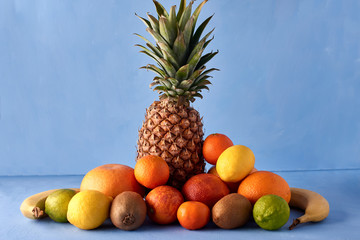 Fresh fruits  on a blue background. Tasty composition of pineapple, mandarin, kiwi, Sicilian orange, lemon, lime and beverages. Exotic drink photography with copy space.