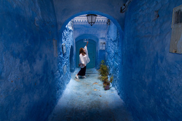 Fototapeta na wymiar A young woman strolls through the streets of Chefchaouen, the blue town in Morocco, between the walls and the blue arches
