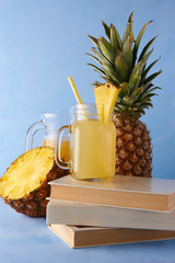 Fresh fruit and juices with books on a blue background. Tasty composition of pineapple and beverages. Exotic drink photography with copy space.
