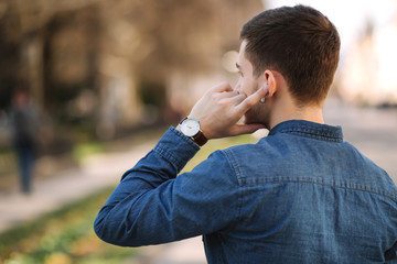 Back view of man usin wireless headphones. Man put his finger on headphone