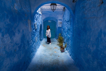 A young woman strolls through the streets of Chefchaouen, the blue town in Morocco, between the walls and the blue arches