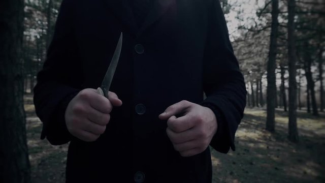 Maniac with knife and sharp blade approaches victim and wants to cut her in woods in close up. Horror in park