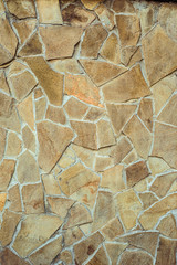 Wall from chipped stone of yellow brown. Decorative vertical texture uneven wall surface
