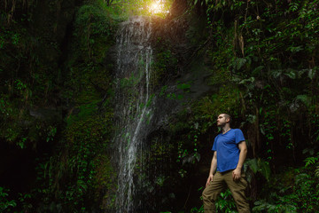 A brave explorer stands in the middle of the dark jungle near the waterfall and looks up at the ray...