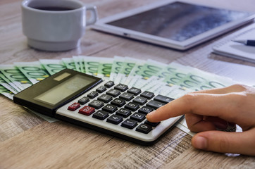 Female hand is counting something on the background of the wooden table, calculator 