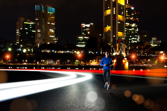 Young Sports Man Running on the Night Road with Cars Light Trails. Healthy Lifestyle and Urban Sport Concept.