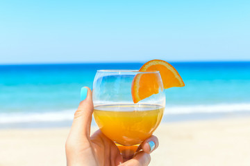 Orange juice in woman hands on the beach with sea background 