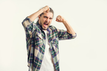 Portrait of a young man screaming and gesturing showing negative emotions while standing on a light background.