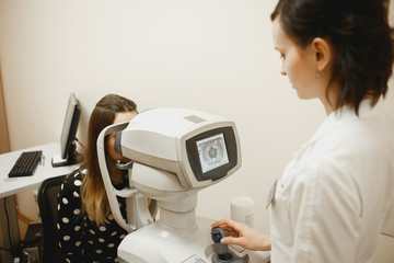 Attractive female doctor ophthalmologist is checking the eye vision of patient in modern clinic.