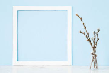 Fresh fluffy willow twigs in glass vase on wooden shelf at pastel light blue wall. Empty place for...