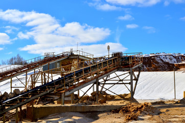 Naklejka premium Mining plant in the open sand pit for the production of crushed stone, sand and gravel. View of the crushing machines and conveyor belts against the blue sky with clouds