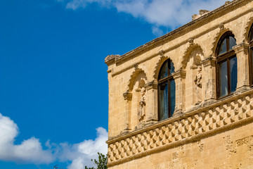 Wall figurine sculpture, architectural detail from the historic center of Matera, Italy, Basilcata region, low point of view from below, scenery summer day with puffy white clouds