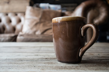 Tynemouth / Great Britain - April 6, 2019: Earthen ware mug cup on a rustic table with empty sofa behind.  Coffee or Tea Shop scene