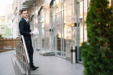 Young business man with documents and mobile phone near of modern building.