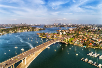 Concrete arch of Gladesville bridge over Parramatta river in Sydney Inner West with view of distant Sydney city CBD and local marina docked floating yachts.