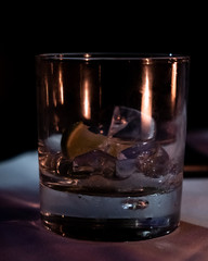 An empty glass of Gin and Tonic stands on a dimly lit white table cloth