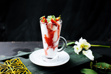 Photo of a glass with icecream with slice of strawberry on a dark background