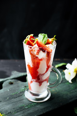 A glass with icecream decorated with slice of strawberry and mint