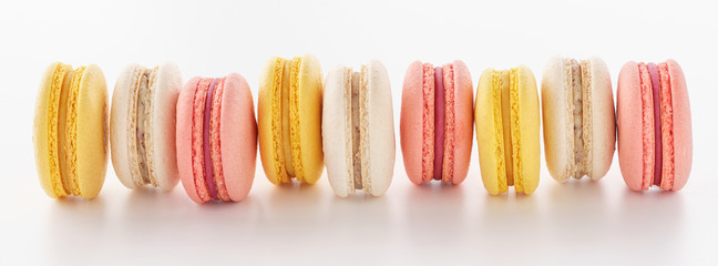 Pink, yellow and white macarons in a row on white background.