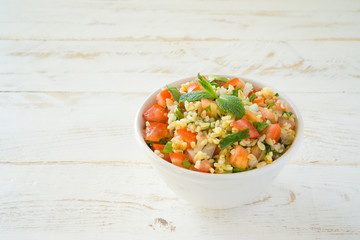 Tabbouleh salad with bulgur, parsley, mint  and tomato in a white bowl on a wooden white rustic background with copy space for text. Traditional Lebanese Arabic Salad
