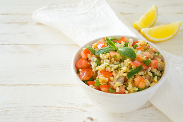 Tabbouleh salad with bulgur, parsley, mint  and tomato in a white bowl on a wooden white rustic background with copy space for text. Traditional Lebanese Arabic Salad