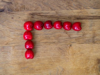 cherry on wooden background as a letter