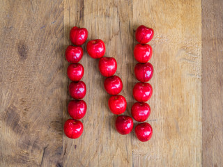 cherry on wooden background as a letter
