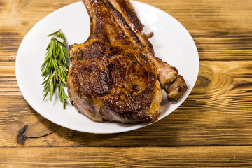 Roasted beef rib eye steak on bone with rosemary in white plate on wooden table