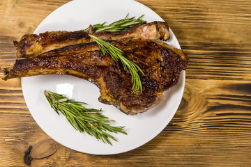Roasted beef rib eye steak on bone with rosemary in white plate on wooden table