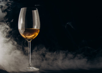 a glass of white wine on a black background. the smoke from the hookah envelops the glass. rest,...