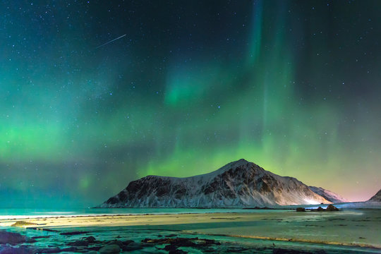 Northern lights at night in the beg lonely beach with big mountains