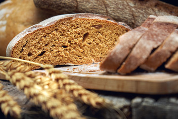 Sliced rye round bread and wheat ears on the old wooden table