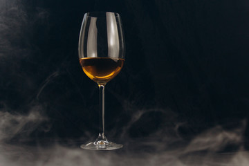 a glass of white wine on a black background. the smoke from the hookah envelops the glass. rest, holiday. alcoholic drink closeup. white fog