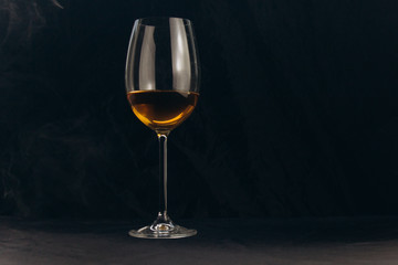a glass of white wine on a black background. the smoke from the hookah envelops the glass. rest, holiday. alcoholic drink closeup. white fog