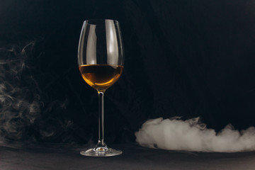 a glass of white wine on a black background. the smoke from the hookah envelops the glass. rest, holiday. alcoholic drink closeup. white fog