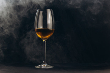 Obraz na płótnie Canvas a glass of white wine on a black background. the smoke from the hookah envelops the glass. rest, holiday. alcoholic drink closeup. white fog