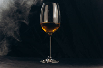 a glass of white wine on a black background. the smoke from the hookah envelops the glass. rest, holiday. alcoholic drink closeup. white fog