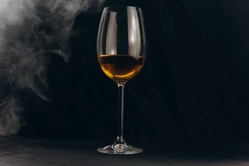 Fotobehang a glass of white wine on a black background. the smoke from the hookah envelops the glass. rest, holiday. alcoholic drink closeup. white fog © Yuliia