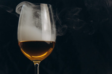 a glass of white wine on a black background. the smoke from the hookah envelops the glass. rest, holiday. alcoholic drink closeup. white fog in a glass. fog