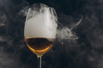 a glass of white wine on a black background. the smoke from the hookah envelops the glass. rest, holiday. alcoholic drink closeup. white fog in a glass. fog