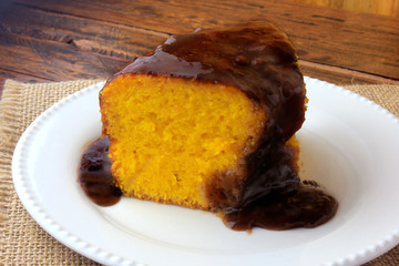 slice of carrot cake with chocolate coating on white ceramic plate on rustic wooden table