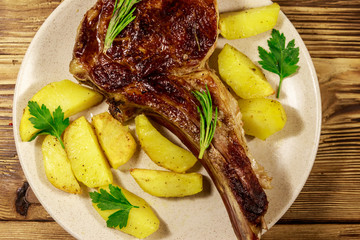 Roasted beef rib eye steak on bone with baked potatoes and herbs on wooden table