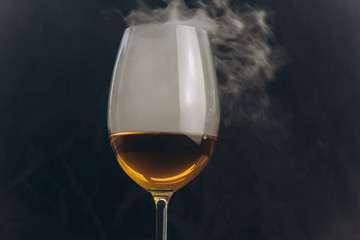 a glass of white wine on a black background. the smoke from the hookah envelops the glass. rest, holiday. alcoholic drink closeup. white fog in a glass. fog