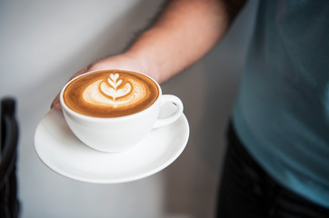 Hand holding latte or Cappuccino with frothy foam, coffee cup top view in cafe.
