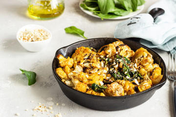 Roasted cauliflower with spinach, raisin and nuts in a cast-iron pan. Light grey background. Copy space. Healthy vegan food.