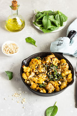 Roasted cauliflower with spinach, raisin and nuts in a cast-iron pan. Light grey background. Copy space. Healthy vegan food.